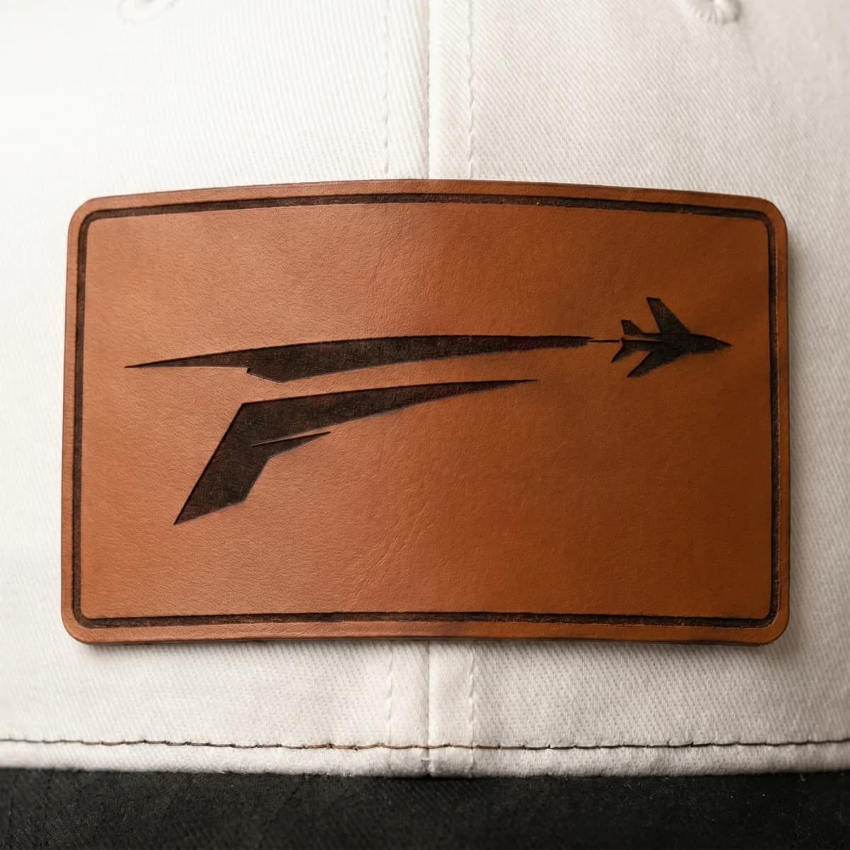 Cognac leather patch on The Icon with engraved F and jet mark, centered on white front panel