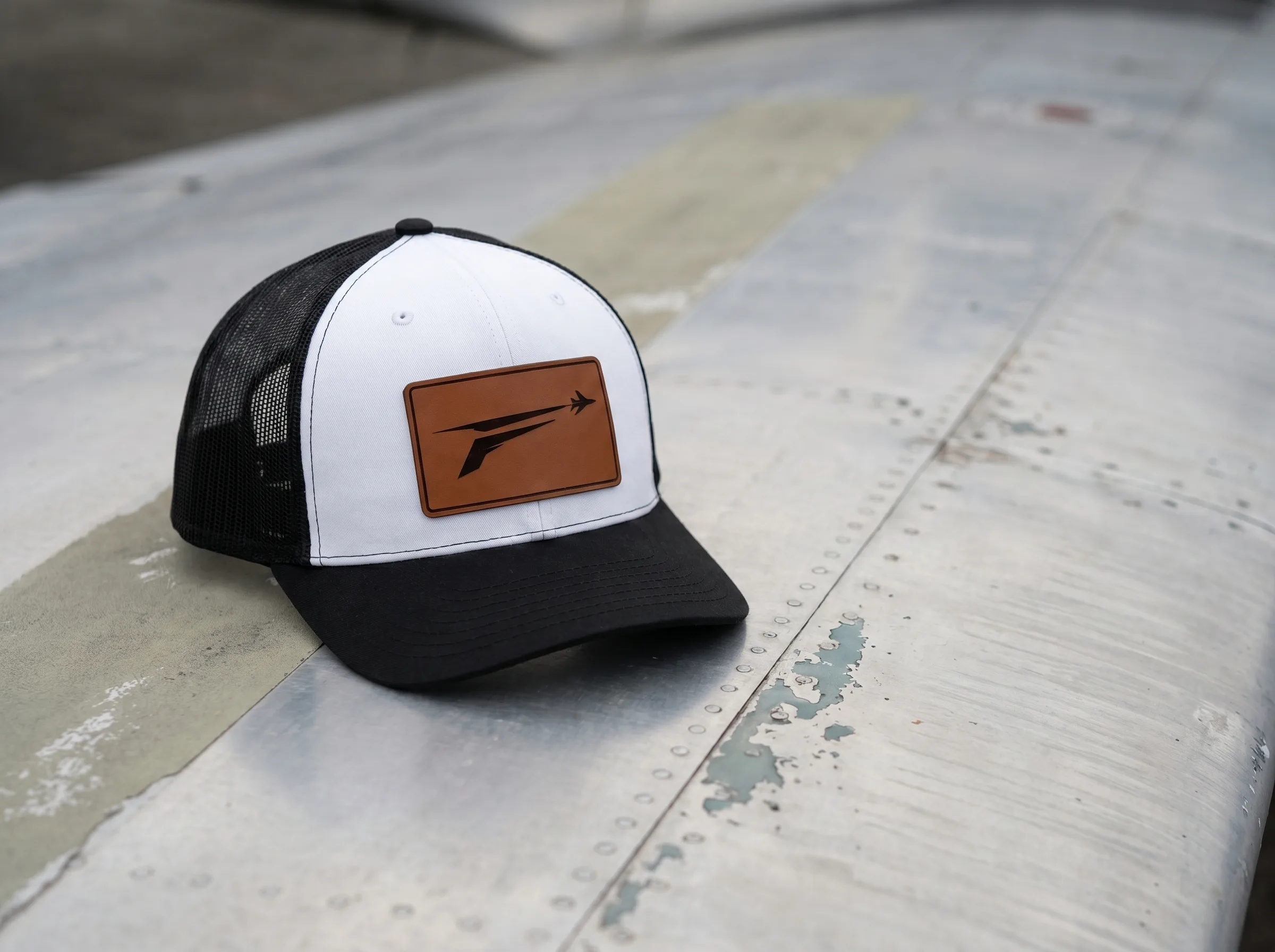 The Icon trucker hat resting on a weathered aluminum aircraft wing on the ramp.