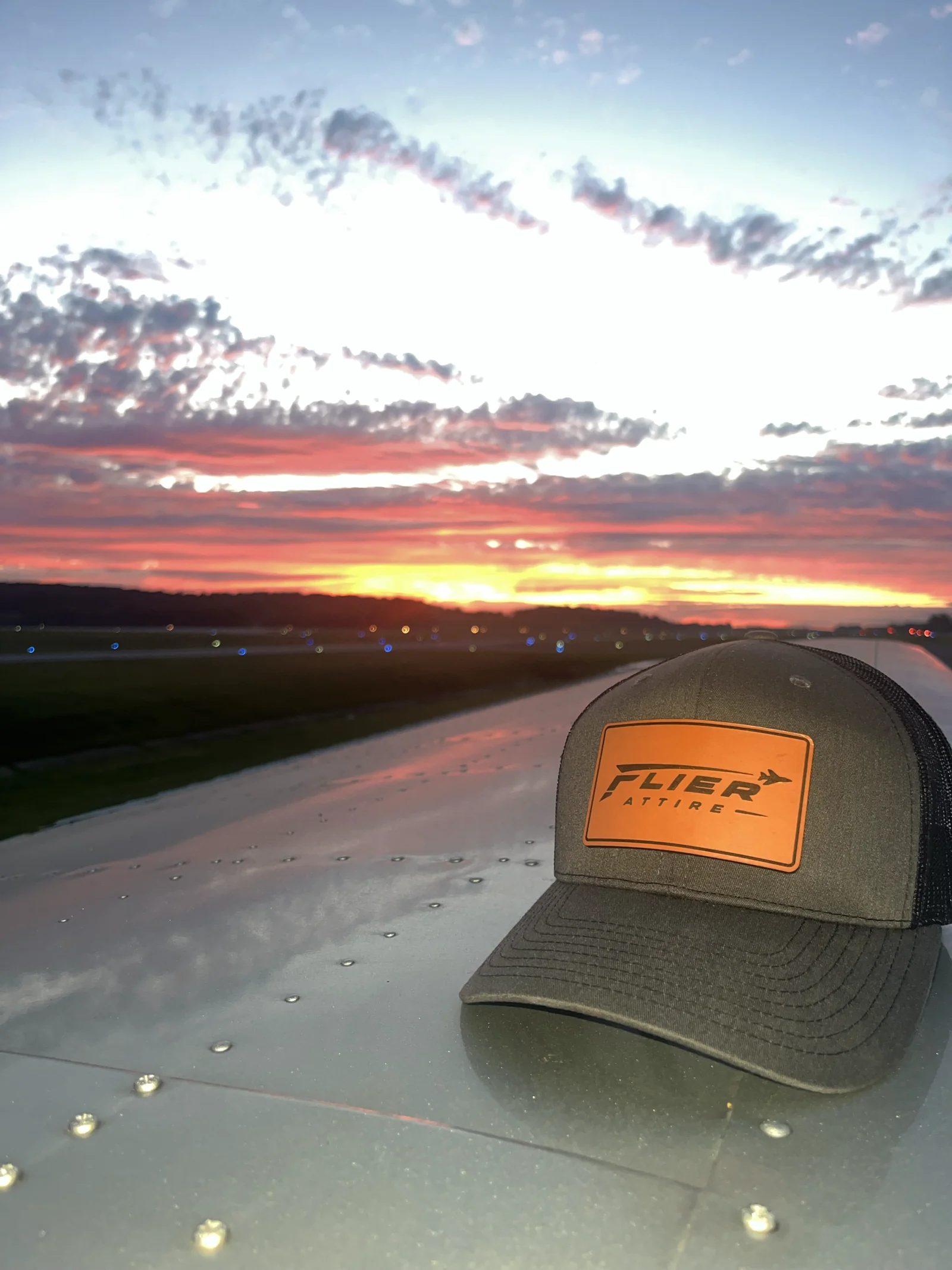 Flier Attire Signature trucker hat resting on an aircraft wing on the tarmac at sunset